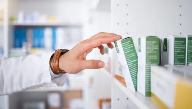 A pharmacist's hand taking a box of medicine off a shelf.