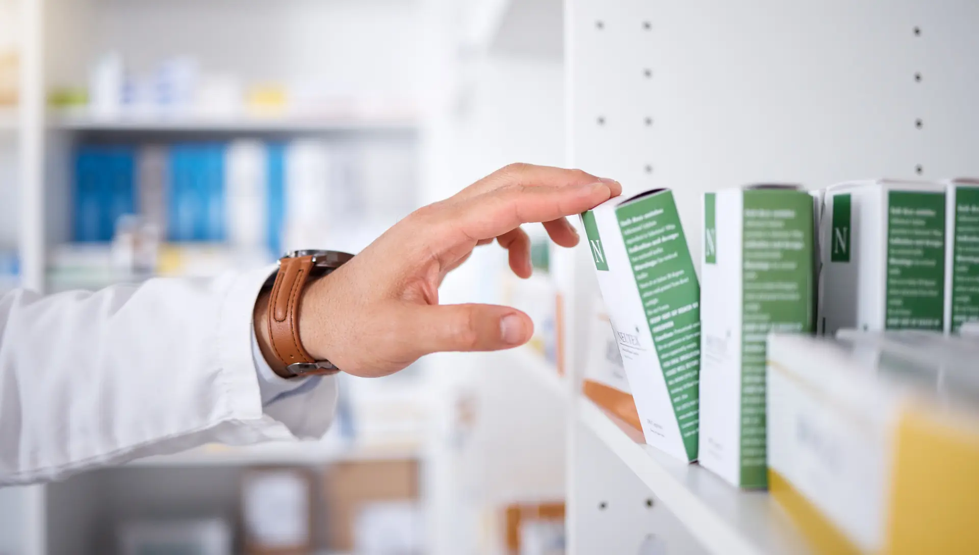 A pharmacist's hand taking a box of medicine off a shelf.